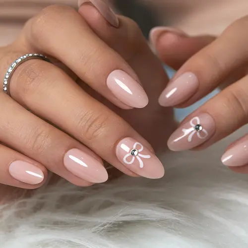 Elegant Nude Pink Almond Nails with Delicate White Bow Design and Subtle Rhinestone Accent – Minimalist yet Chic Nail Art for Everyday Wear, Bridal Looks, Feminine Touch with a Hint of Sparkle for Graceful and Timeless Style